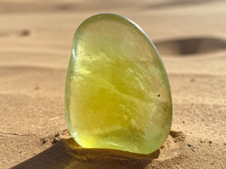 Pale yellow translucent stone standing on sandy ground.