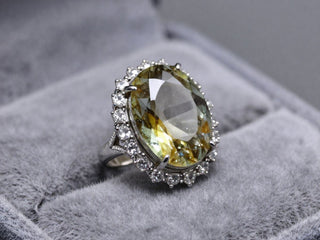 Silver ring with a large pale green gemstone and sparkling halo setting.
